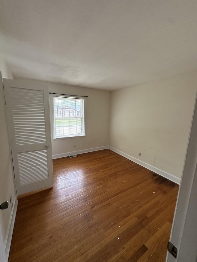 unfurnished room featuring baseboards, wood finished floors, and visible vents