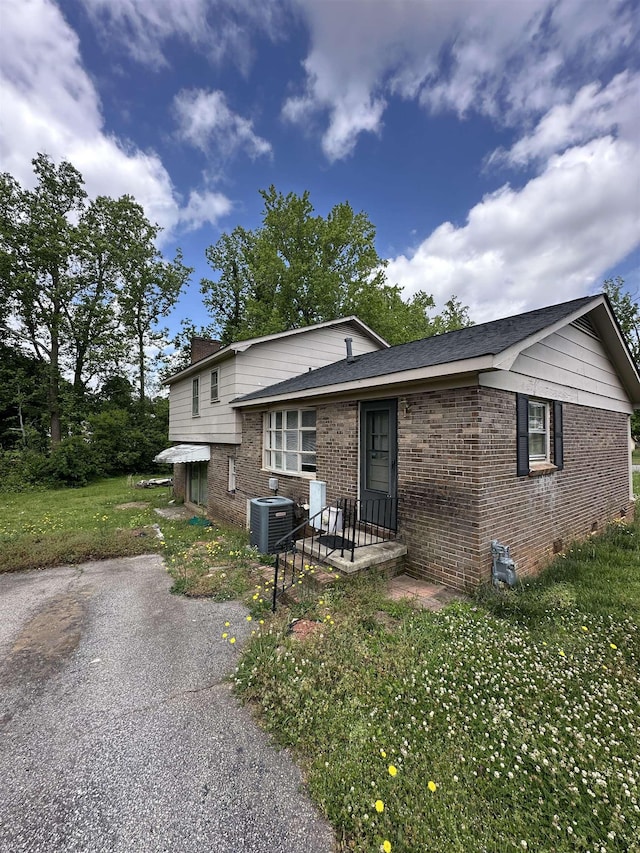 split level home with central air condition unit, brick siding, crawl space, and a front lawn