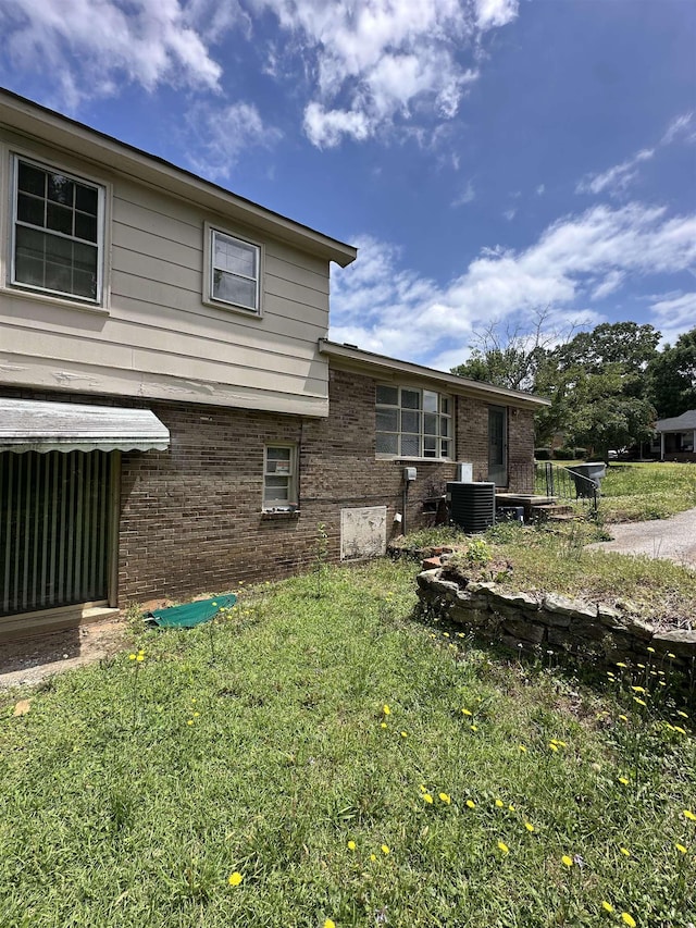 view of side of home with central air condition unit, brick siding, and a yard