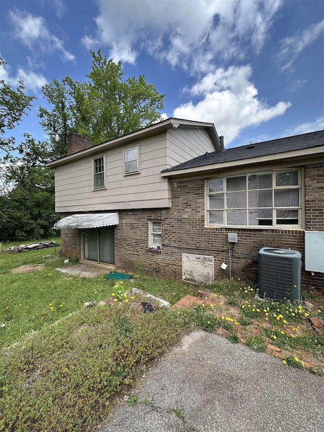 view of side of home with a yard, a chimney, cooling unit, and brick siding