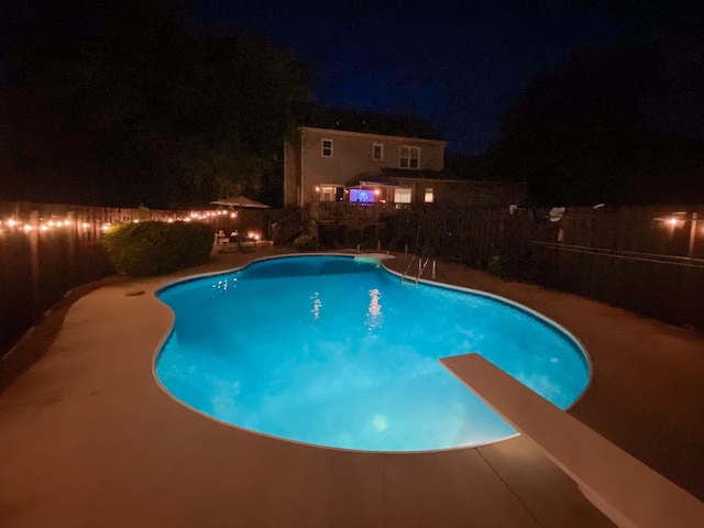pool at night with a fenced in pool, a fenced backyard, and a patio area