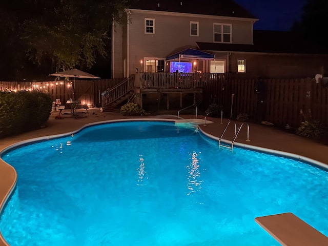 pool at night with a fenced backyard, a fenced in pool, and a wooden deck