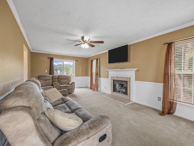 living area with a textured ceiling, ceiling fan, wainscoting, and a tiled fireplace