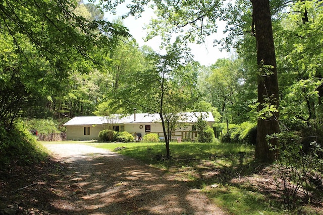 ranch-style house with a view of trees and dirt driveway