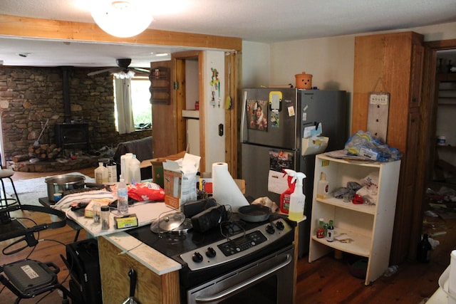 kitchen featuring a wood stove, appliances with stainless steel finishes, wood finished floors, and ceiling fan