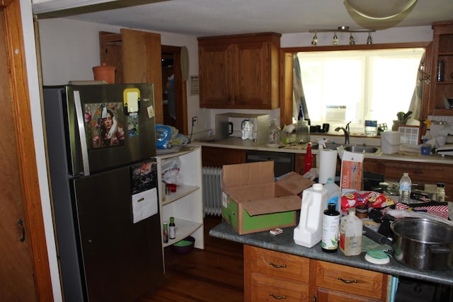 kitchen with brown cabinetry, a sink, freestanding refrigerator, radiator, and dark wood-type flooring