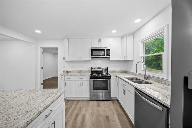 kitchen featuring light stone countertops, white cabinetry, a sink, light wood finished floors, and stainless steel appliances