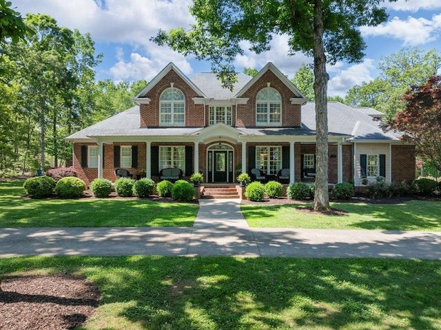 view of front of home with a porch, brick siding, and a front yard