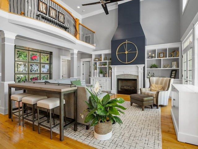 living room featuring ceiling fan, a premium fireplace, light wood-style flooring, a towering ceiling, and ornamental molding