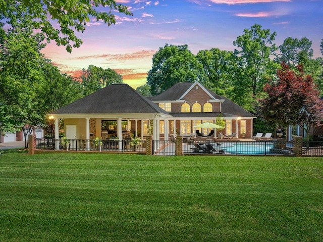 back of house at dusk featuring a lawn, fence, a fenced in pool, and a patio