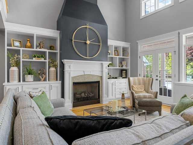 living area with french doors, light wood finished floors, a towering ceiling, and a premium fireplace