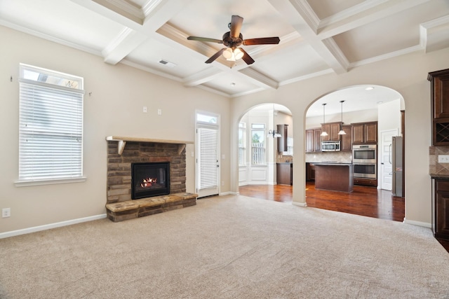 unfurnished living room with ceiling fan, beam ceiling, a fireplace, dark colored carpet, and coffered ceiling
