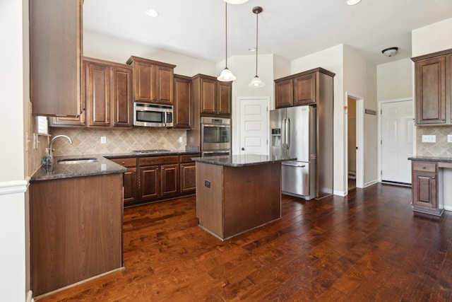 kitchen featuring decorative backsplash, a kitchen island, dark stone counters, a sink, and appliances with stainless steel finishes