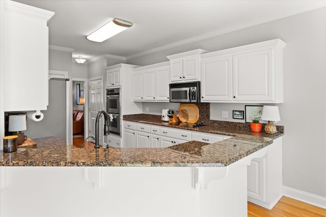 kitchen featuring crown molding, a peninsula, dark stone counters, a sink, and appliances with stainless steel finishes