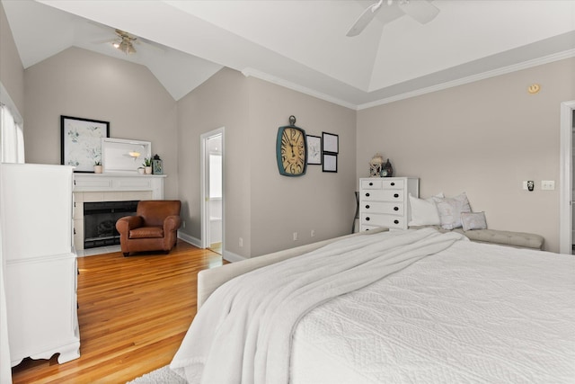 bedroom with a tile fireplace, multiple windows, lofted ceiling, and light wood-style floors