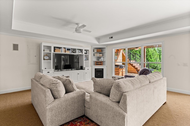 carpeted living area with baseboards, ceiling fan, a tray ceiling, and a fireplace