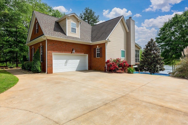 view of property exterior featuring roof with shingles, an attached garage, brick siding, a chimney, and driveway