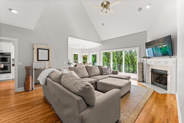 living room with high vaulted ceiling, recessed lighting, a tile fireplace, light wood finished floors, and ceiling fan with notable chandelier