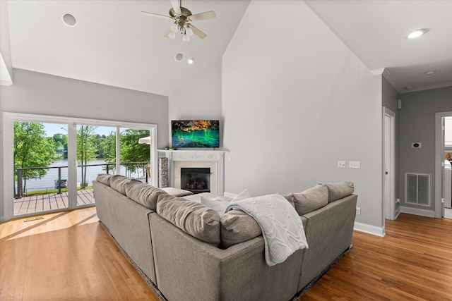 living area featuring a fireplace, high vaulted ceiling, baseboards, wood finished floors, and visible vents