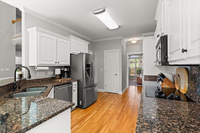 kitchen featuring appliances with stainless steel finishes, a sink, light wood finished floors, ornamental molding, and white cabinetry
