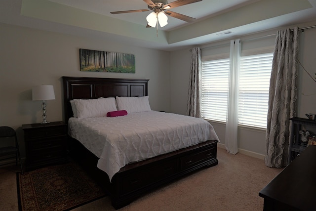 bedroom featuring light colored carpet, baseboards, ceiling fan, and a tray ceiling