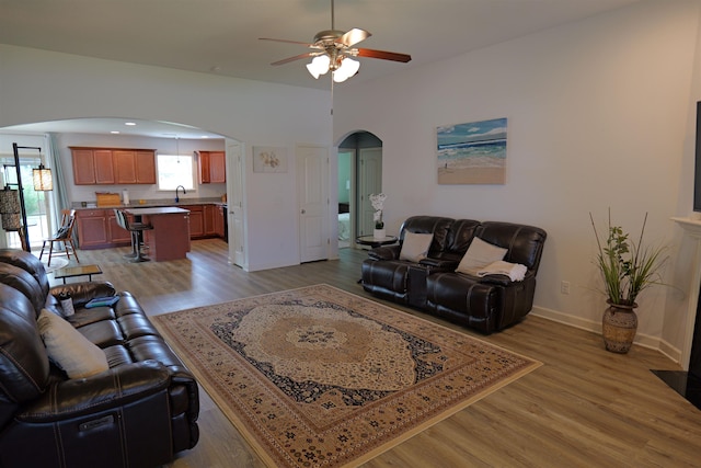living room with arched walkways, ceiling fan, baseboards, and light wood finished floors