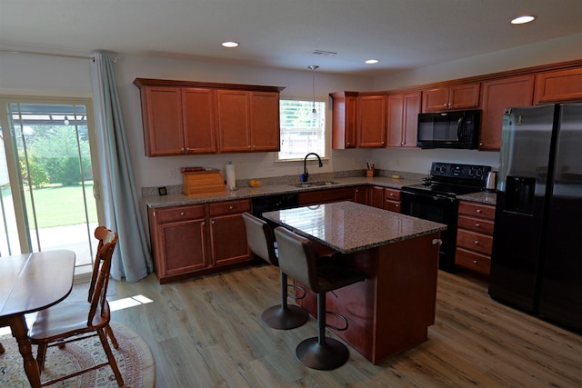 kitchen with light wood-type flooring, a sink, stone countertops, and black appliances