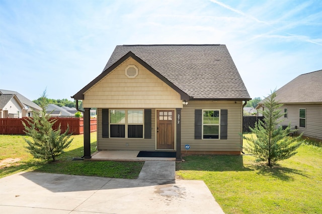 view of front of property featuring covered porch, roof with shingles, fence, and a front yard