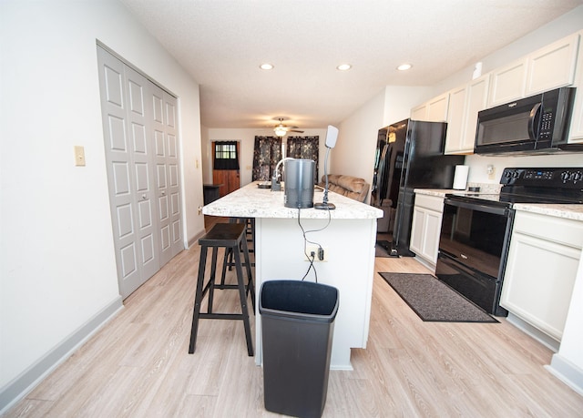 kitchen with light wood-style floors, black appliances, recessed lighting, and an island with sink