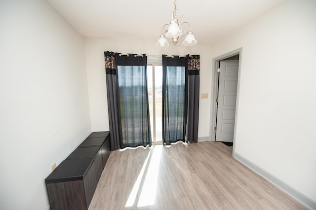 unfurnished room featuring baseboards, light wood finished floors, and a chandelier
