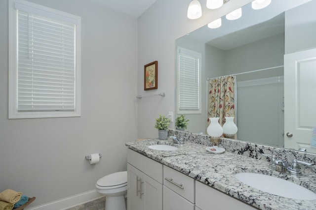 bathroom with double vanity, toilet, baseboards, and a sink