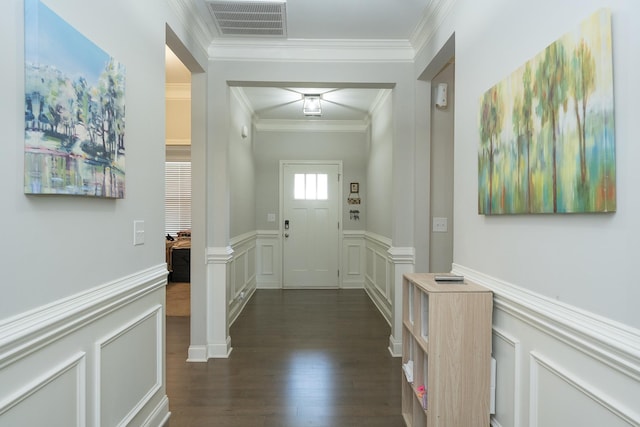 doorway featuring visible vents, crown molding, wainscoting, a decorative wall, and dark wood finished floors
