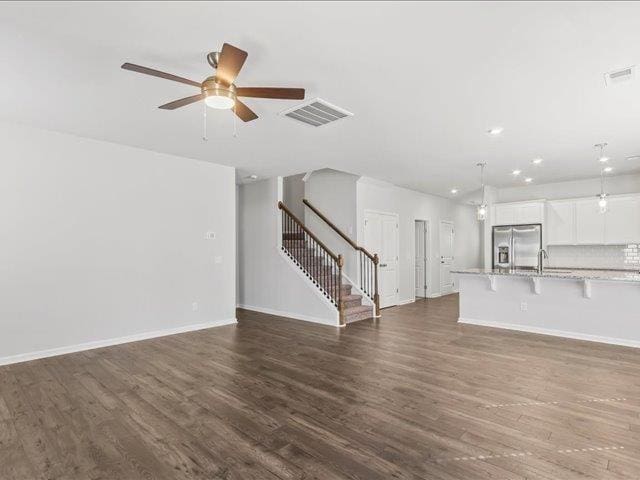 unfurnished living room with a ceiling fan, visible vents, baseboards, stairs, and dark wood-type flooring
