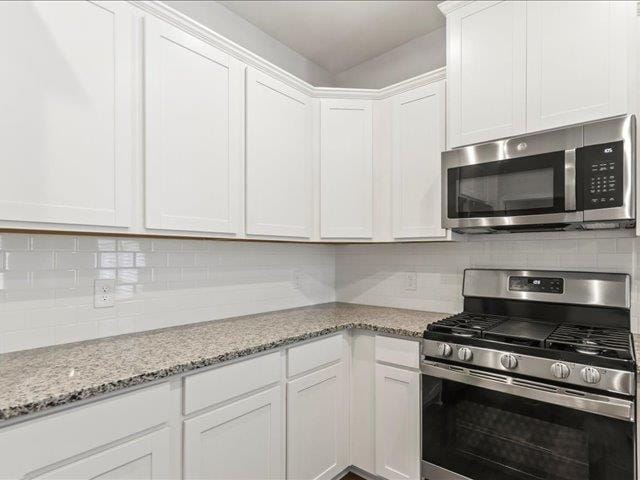 kitchen with light stone counters, white cabinets, backsplash, and stainless steel appliances