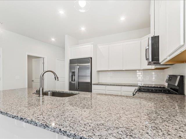kitchen with decorative backsplash, appliances with stainless steel finishes, a sink, light stone counters, and white cabinets