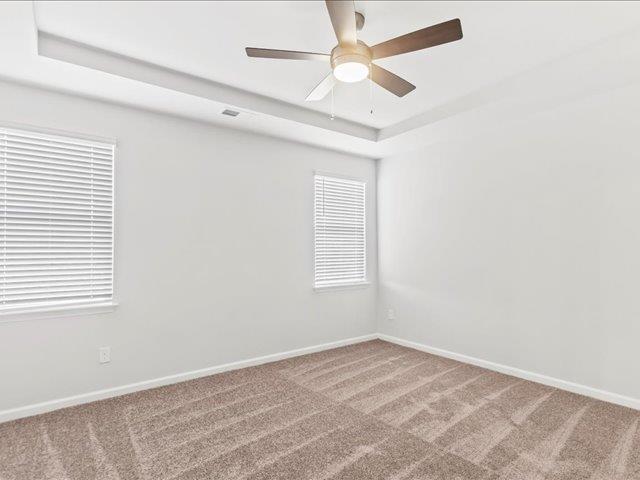 empty room with baseboards, carpet, ceiling fan, and a tray ceiling