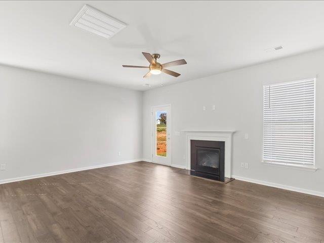 unfurnished living room featuring visible vents, a glass covered fireplace, baseboards, ceiling fan, and dark wood-style floors