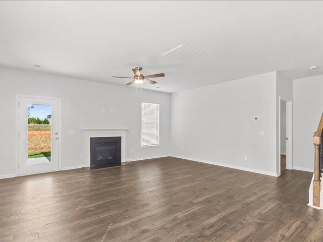 unfurnished living room featuring dark wood-style flooring, ceiling fan, baseboards, and a fireplace