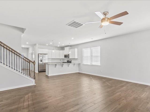 unfurnished living room with visible vents, stairs, baseboards, ceiling fan, and dark wood-type flooring