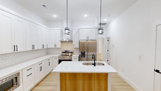 kitchen with wall chimney range hood, a sink, light wood-style flooring, stainless steel appliances, and tasteful backsplash
