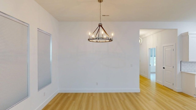 unfurnished dining area with baseboards, visible vents, light wood-style flooring, and a notable chandelier
