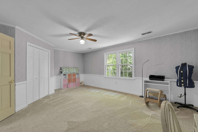 playroom featuring a textured ceiling, carpet, a ceiling fan, visible vents, and ornamental molding