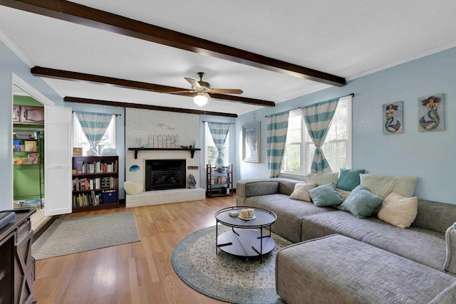 living room with ceiling fan, a brick fireplace, beam ceiling, wood finished floors, and ornamental molding