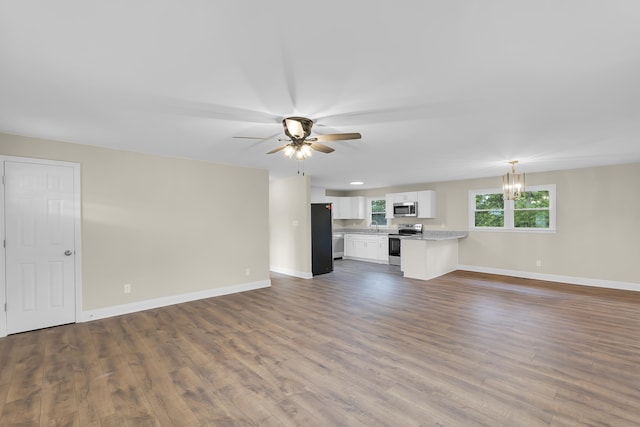 unfurnished living room with baseboards, ceiling fan with notable chandelier, and dark wood-style floors