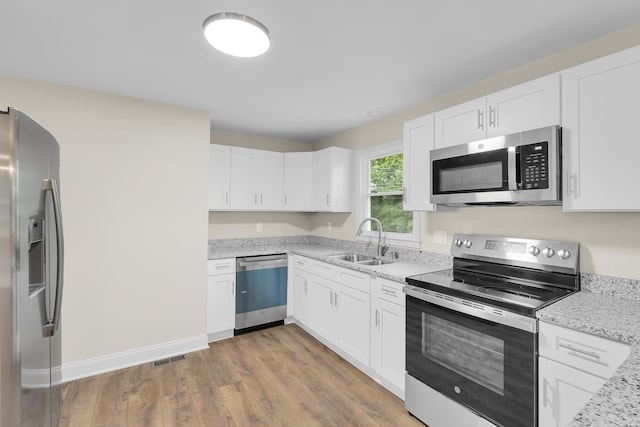 kitchen featuring white cabinets, appliances with stainless steel finishes, light stone counters, a sink, and light wood-style flooring