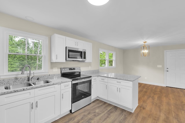kitchen featuring a peninsula, white cabinetry, a chandelier, a sink, and stainless steel appliances