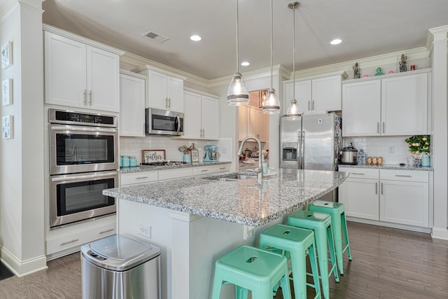 kitchen with white cabinets, a sink, stainless steel appliances, visible vents, and a center island with sink