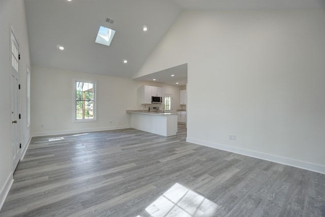 unfurnished living room with high vaulted ceiling, visible vents, a skylight, and baseboards