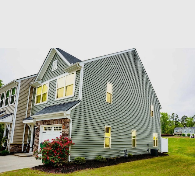 view of side of property with stone siding, a garage, concrete driveway, central air condition unit, and a yard