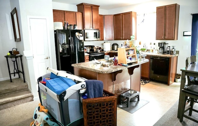 kitchen with light floors, a kitchen breakfast bar, a center island, light countertops, and black appliances